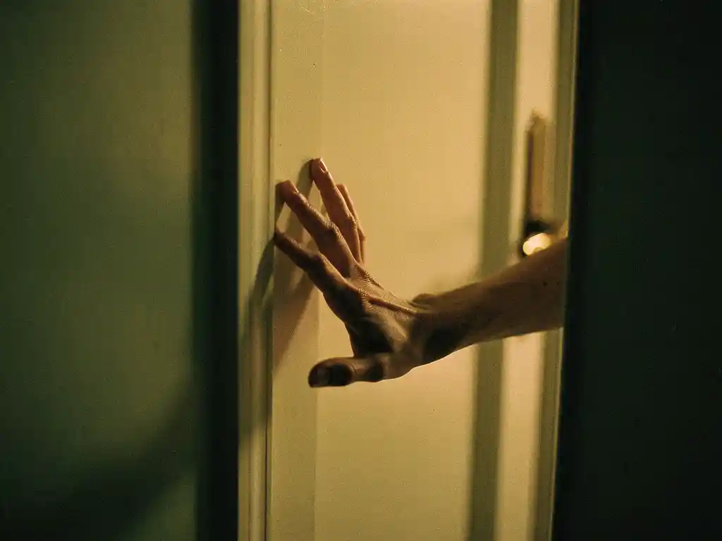 Hand op een gesloten deur in een warmverlichte gang met salie groene muren en zachte amber tinten.